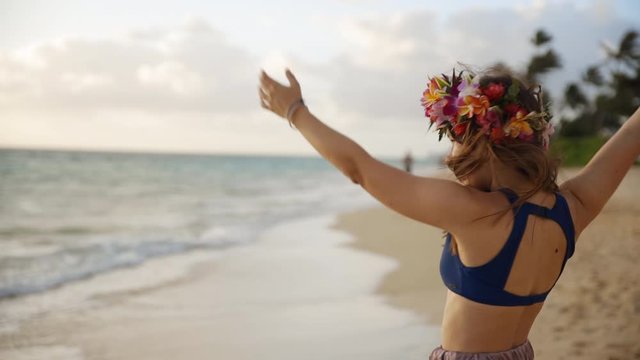Slow motion close up, young woman spinning on beach wearing Hawaii lei