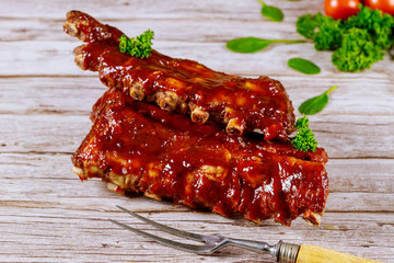 Beef ribs with barbecue sauce and fork on wooden board.