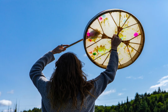 Rear Closeup View Of Young Shamanic Woman Holding Sacred Native Frame Drum With Raised Hands Worshiping In Northern Quebec In Canada