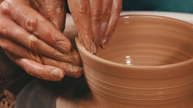 Man's hands sculpting the sides from a pot out from the clay on a potter wheel