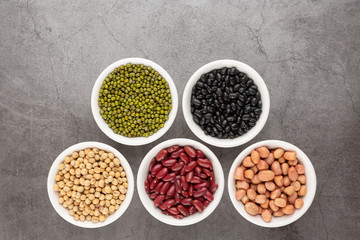Grains or beans, red bean, black bean, green bean, soybean, peanut in the white bowl placed on the black cement floor. Top view.