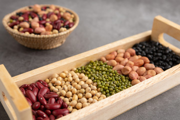 Grains or beans, red bean, black bean, green bean, soybean, peanut in the wooden tray and the wooden basket placed on the black cement floor. High angle view.