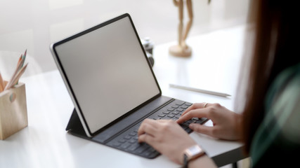 Close up view of female designer typing on blank screen tablet in simple co working space