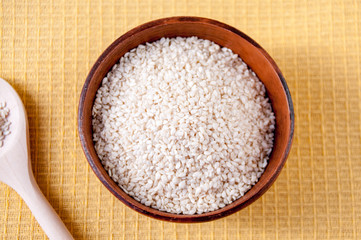 White sesame seeds in a clay Cup and wooden spoon on the table, top view