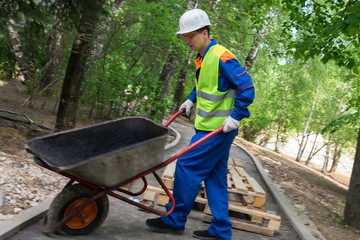 a worker in a helmet carries an empty cart on unfinished roads