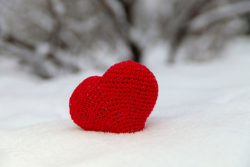 Red heart on white snow in the center of the frame. Close-up of a red knitted heart of thread on a snowdrift of snow in a park.Close-up, horizontal, free space. Valentine's Day concept.