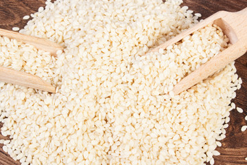 Heap of sesame seeds with wooden scoop on board