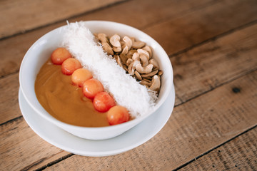 Mango smothie bowl with fruit, coconut flakes and cashew on wooden background.