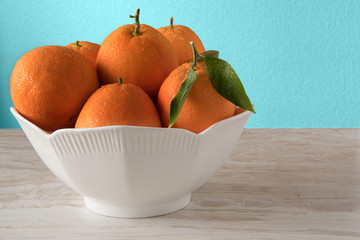Fresh oranges in white porcelain Bowl. Healthy Citrus fruits on blue background. Kitchen Concept