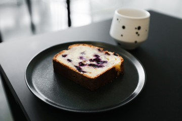 A piece of a fruit cake with berries and a cup of coffee on a black table