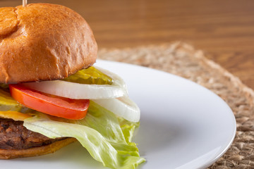 A closeup view of a cheeseburger on a plate, in a restaurant or kitchen setting. The cheeseburger sits on the left side of the frame.