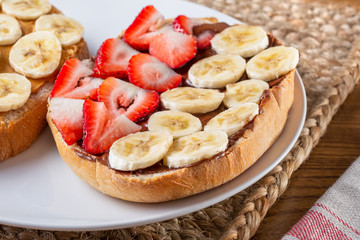 A view of a slice of toast on a plate, featuring hazelnut chocolate spread and fruit toppings, in a restaurant or kitchen setting.