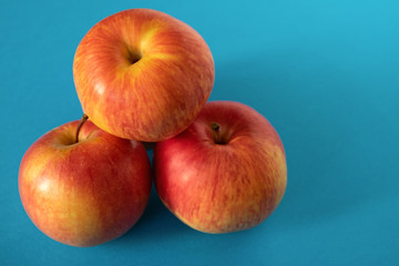 A few juicy ripe yellow-red apples are stacked with a bunch on a blue background. Copy space.