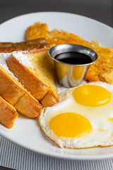 A view of a breakfast plate in a restaurant or kitchen setting, featuring hash browns, sausage links and French toast.