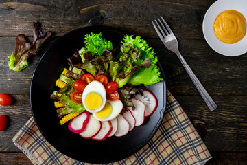 Fresh salad with boiled egg in black dish on wooden table, Tomato and Radish.