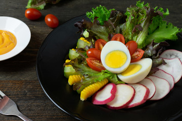 Fresh salad with boiled egg in black dish on wooden table, Tomato and Radish.