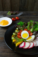 Fresh salad with boiled egg in black dish on wooden table, Tomato and Radish.