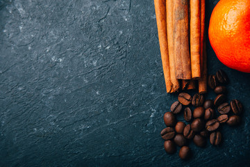 Coffee beans and cinnamon on black background with tangerine