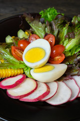Fresh salad with boiled egg in black dish on wooden table, Tomato and Radish.