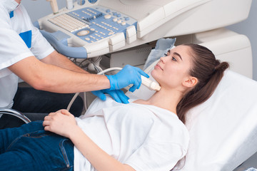 Young woman patient during the ultrasound examination of a thyroid lying on the couch in medical...