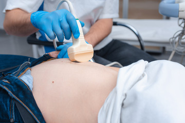 The young doctor makes an ultrasound of the abdominal cavity to a young beautiful girl. Ultrasound...