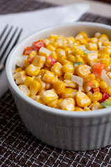 A closeup view of a ramekin bowl of Korean corn salad in a restaurant or kitchen setting.