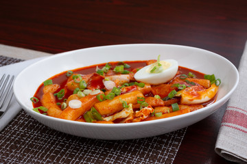 A view of a plate of Korean Tteok-bokki, which is a spicy rice cake dish, in a restaurant or kitchen setting.