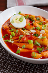 A view of a plate of Korean Tteok-bokki, which is a spicy rice cake dish, in a restaurant or kitchen setting.