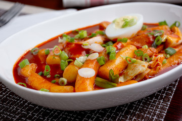 A view of a plate of Korean Tteok-bokki, which is a spicy rice cake dish, in a restaurant or kitchen setting.
