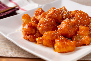 A view of a plate of orange shrimp in a kitchen or restaurant setting.