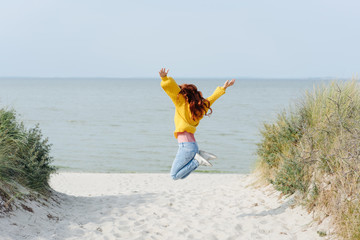 Girl in yellow jumping for joy on the beach
