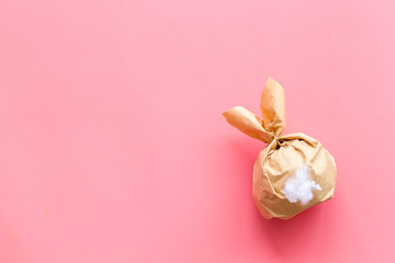 Easter gift in shape of bunny with tail on pink background top-down copy space