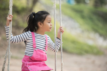 happy little asian girl child having fun to playing in the playground in summer time with smile and laughing healthy, Adorable girl having fun on a swing on summer. happy vacation lifestyle concept.