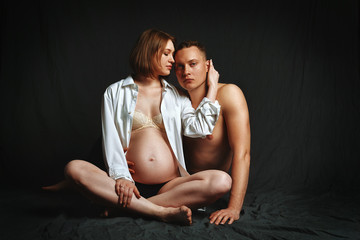 Pregnant couple posing for the camera on a brown background, low key. Fashion Pregnancy Concept. Copy space, brown background.