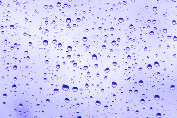 beautiful raindrops on glass window while raining with different texture with violet color blurred background.