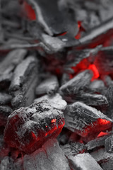 Closeup side view of bright smoldering charcoals in a bonfire with shallow depth of field. Abstract modern trendy texture background