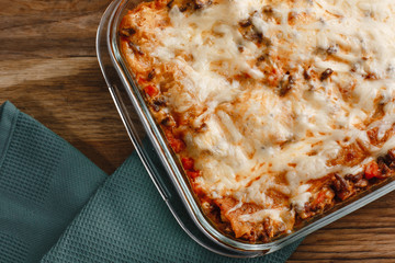 Traditional Italian lasagna with vegetables, minced meat, tomatoes and cheese on a fabric and wooden background with wine