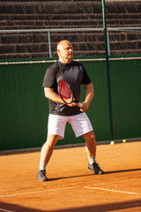 A bald man plays tennis on the court on a sunny day. Health and activity. Vertical.