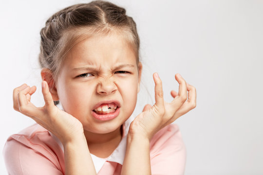 The school-age girl in a pink sweater is angry. White background. Close-up.