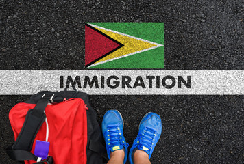 Man in shoes with bag standing next to line with word IMMIGRATION and flag of Guyana on asphalt road