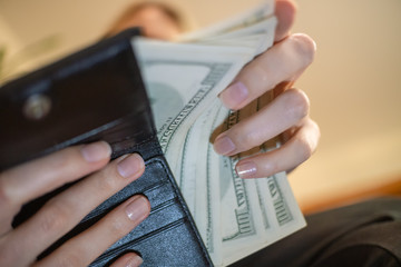 Hands of a girl with a black wallet and dollars close-up.