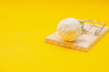 Raffaello candy in a mousetrap on a yellow background. Concept of health, diet