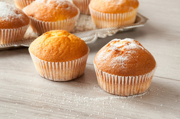 Fresh homemade delicious muffins are taken out of the oven and they cool on the kitchen table. Muffins sprinkled with sugar. Sweet dessert.