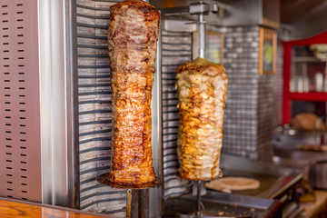 Two rotating skewered chicken and lamb meat grilled in stainless steel grill and ready to serve in...