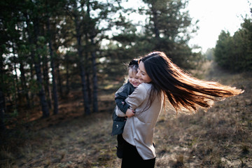 Young beautiful mom turns over daughter in her arms on the forest background. Parenthood. Mom hugs daughter