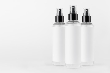 Three tall transparent spray dispenser bottles for cosmetics product with white label on white background, mock up for branding, design.