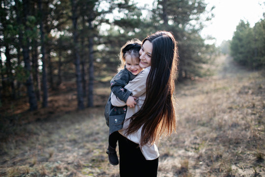 Young beautiful mom holds daughter in her arms and smiles on the forest background. Parenthood. Mom hugs daughter