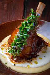 Roast lamb shank with green leaves in a plate on a dark wooden background. Concept for menu design