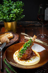 Roast lamb shank with green leaves in a plate on a dark wooden background. Concept for menu design, copy space