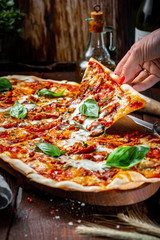 Hand takes a piece of Long pizza Margarita with sun-dried tomatoes and Basil on a wooden Board....